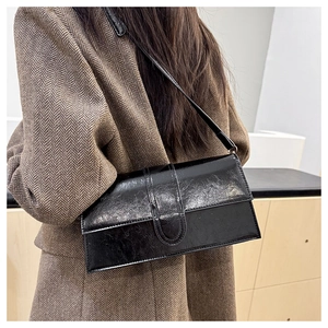 Chic black polished baguette shoulder bag styled on a model wearing a brown blazer