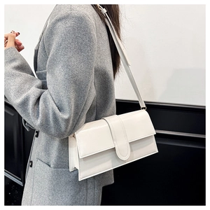 Close-up of minimalist white leather crossbody bag with wide buckle on grey blazer
