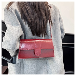 Detail of burgundy glossy leather shoulder bag worn with a grey blazer for a modern look