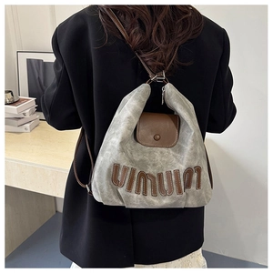 Detail of grey canvas backpack with brown leather flap and letter embroidery on model