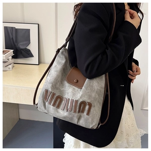 Detail der grauen Canvas-Hobo-Tasche mit Leder-Buchstaben-Patch und braunem Trageriemen