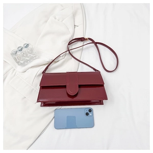 Flat lay of a burgundy patent leather baguette bag with slender strap on white fabric