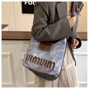 Detail of blue denim tote bag with leather straps and 3D embossed lettering on model