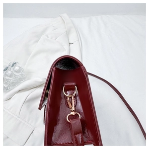 Detailed side view of dark red patent leather bag with gold D-ring hardware and gusset