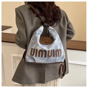Detail of blue denim shoulder bag featuring brown leather trim and retro letter patches