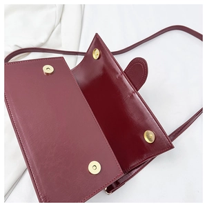 Detail of dark red crossbody bag showing gold magnetic snaps and clean interior space
