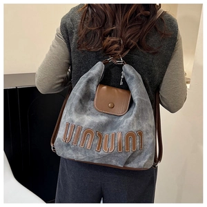 Detail eines graublauen Canvas-Rucksacks mit brauner Lederklappe und Buchstaben-Patch
