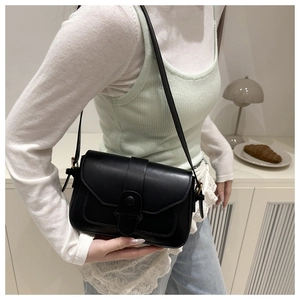Détail d'un sac bandoulière minimaliste en cuir noir mat porté avec une tenue décontractée