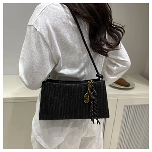Detalle del bolso de hombro trenzado negro con dije de raqueta dorada y borla suave