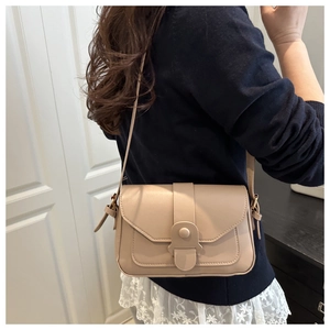 Dettaglio di una borsa a tracolla beige con trama in pelle opaca e fibbia tonda