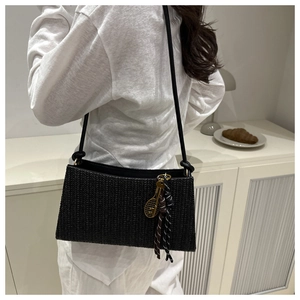 Detalle de bolsa tote tejida negra con colgante de raqueta de tenis dorado