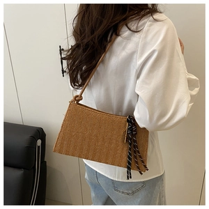 Detalle de un bolso shopper trenzado marrón con borla a rayas y correas finas para hombro