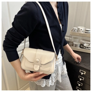 Close-up of a cream-colored leather flap bag with magnetic snap and wide decorative strap