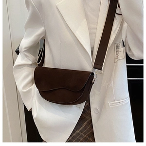 Detail of dark brown suede saddle bag with stylish wide strap on a white blazer