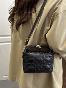 Black heart-quilted crossbody bag with gold twist lock on khaki coat model outfit