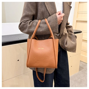 Brown lychee leather tote bag shown styled on a shoulder with a textured blazer