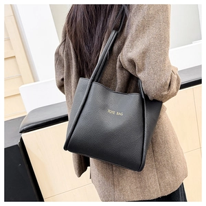 Detail of black lychee grain tote bag with gold lettering shown on a model's shoulder