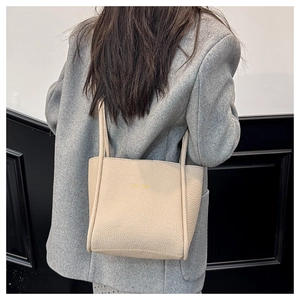 Close-up of beige lychee grain leather tote bag with yellow TOTE BAG print on the side