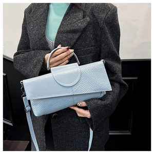 Close-up of light blue crocodile embossed handbag with metal circular handle on model