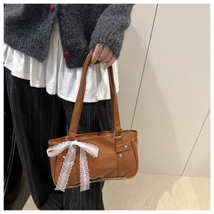 Détail du sac sous le bras en cuir marron vintage avec une breloque en dentelle blanche