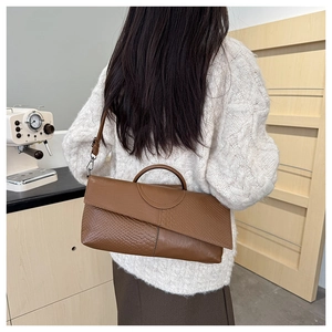 Brown crocodile texture clutch bag with top handle and shoulder strap worn by a model
