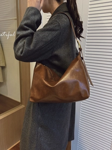 Large brown leather tote bag worn over the shoulder with a stylish gray wool coat