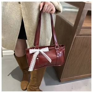 Détail du sac à bandoulière en cuir verni bordeaux avec nœud en dentelle blanche et rivets