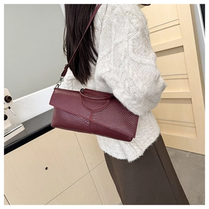 Close-up of burgundy crocodile pattern handbag with metal handle and asymmetric flap design