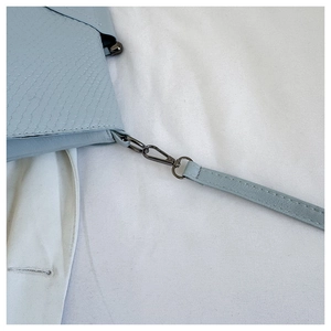 Detail of light blue embossed leather bag showing dark grey metal hardware and shoulder strap
