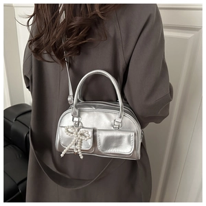 Detail of silver metallic crossbody bag featuring twin flap pockets and a pearl bow charm