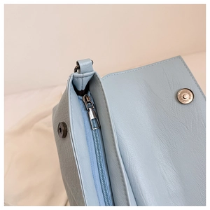 Detail of the sky blue leather bag showing silver metal zipper and magnetic snap closure
