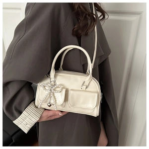 Close-up of cream underarm bag featuring decorative pearl bow and heart charm details