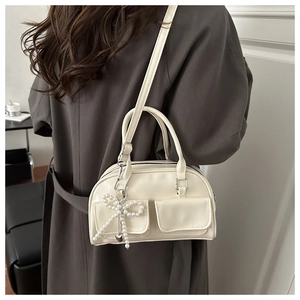 Detail of cream multi-functional handbag with pearl bow charm and dual front flap pockets