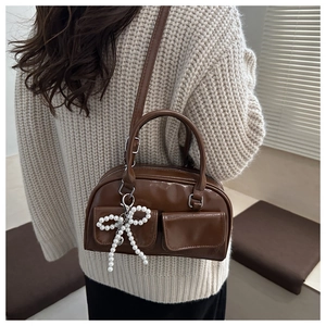 Detail of a brown leather Boston bag featuring a white pearl bow charm and shoulder strap