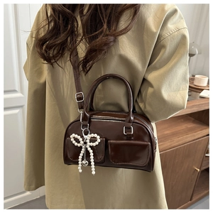 Detail of a brown glossy leather crossbody bag with pearl bow pendant and utility pockets
