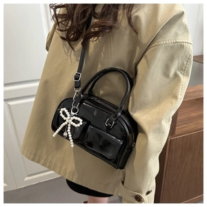 Close-up of black patent leather bowling bag with twin front pockets and pearl bow charm