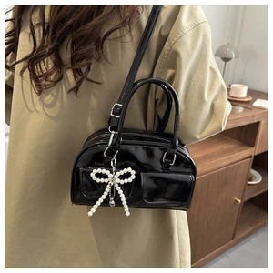Detail of glossy black patent leather handbag with pearl bow charm and twin handles