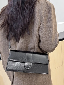 Chic black glossy patent leather shoulder bag for women worn with a stylish blazer