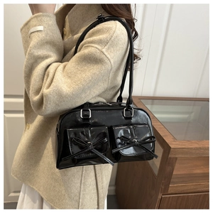 Detail of a shiny black patent leather shoulder bag featuring two decorative front bows