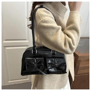Detail of a shiny black patent leather underarm bag with double bow accent pockets