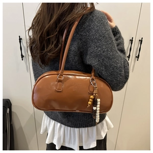 Detail of a brown leather underarm bag featuring a wood bead charm and brand embossing