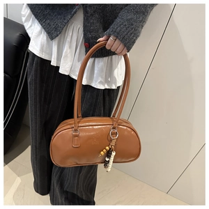 Close-up of caramel brown barrel shoulder bag with fashion text and bohemian bead tassel