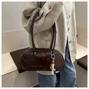 Close-up of dark brown leather handbag featuring fashion text and beaded charm detail