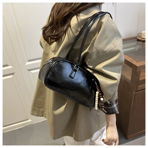 Detail of black glossy leather underarm bag with decorative pearl charm and logo