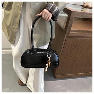 Detail of glossy black baguette bag with fashion lettering and wood bead charm