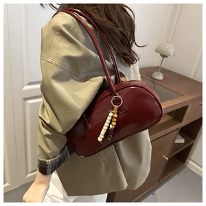 Detail of burgundy glossy leather underarm bag with wooden bead charm and embossed logo