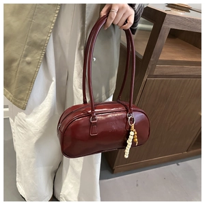 Detail of burgundy glossy leather shoulder bag with beaded charm and embossed text