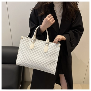 Gros plan d'un sac cabas crème avec motifs M gris et boucles de poignée en métal