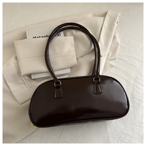 Close-up of a glossy dark brown baguette bag with double straps on a cream blazer