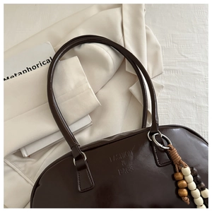 Detailed view of glossy dark brown leather bag with wooden bead charm and embossed logo